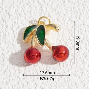 Macro shot of gold-plated cherry charm with red resin fruits and green leaves