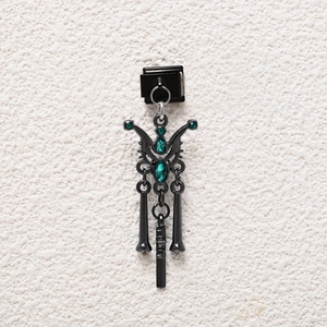 Macro detail of gothic black metal charm with green crystals and skeletal dangles