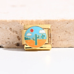 Macro view of gold Italian charm with enamel desert landscape and cactus pattern