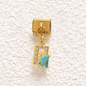 Close-up of golden Italian charm link with rectangular blue gemstone and clear zircons