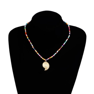 Détail de perles colorées avec un pendentif coquillage doré sur un collier d'été