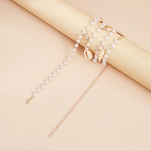 Detail of summer beach body chain with white pearls and gold seashell charms