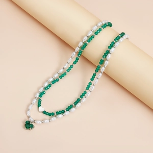 Détail du collier superposé avec perles blanches, cristaux verts et pendentifs cœurs
