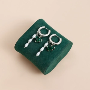Détail de boucles d'oreilles créoles avec perles blanches et pierre précieuse verte
