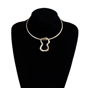 Dettaglio della collana rigida dorata con pendente geometrico su busto nero