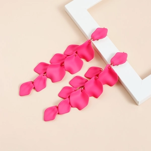 Dettaglio di orecchini a petalo lungo rosa rosa appesi a una cornice in legno bianco