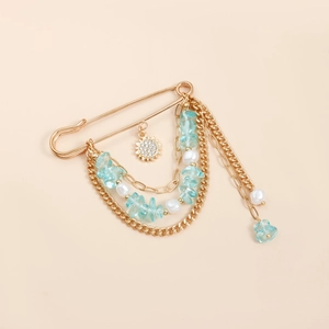Broche bohème dorée avec pierres bleu clair, perles et pendentif soleil sur fond beige