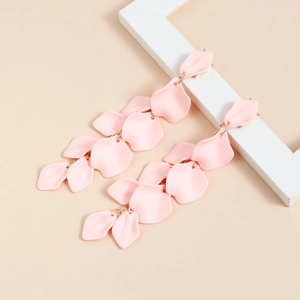 Dettaglio degli orecchini a pendente con petali rosa opachi su sfondo beige delicato
