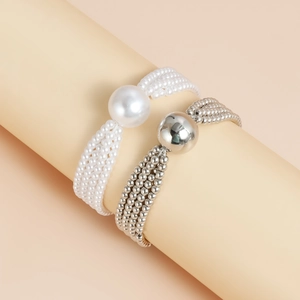 Detail of layered white pearl and silver metal bead necklaces on a soft beige pedestal