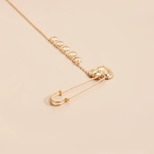 Detail of polished golden safety pin brooch featuring a delicate chain with five heart charms