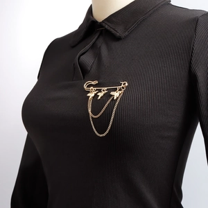 Golden safety pin brooch with bird charms and double chains on black knit shirt