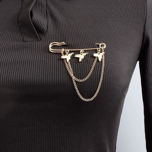 Detailed view of a gold safety pin brooch with bird charms and tassel chains on fabric