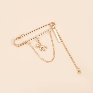 Detail of a gold safety pin brooch featuring a bear charm and elegant hanging chains