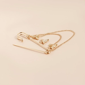 Detailed view of a gold safety pin brooch featuring layered chains and bird pendants