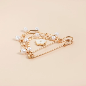 Close-up of golden brooch pin featuring layered chains, white pearls, and flower charm