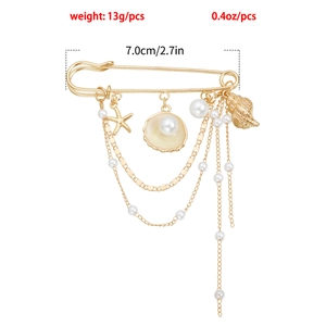 Détail d'une broche océan dorée avec étoile de mer, coquillage et perles sur fond blanc
