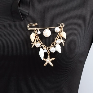 Broche marine dorée ornée de coquillages et d'étoiles de mer sur tissu noir texturé