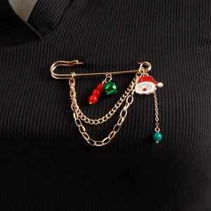 Detail of Christmas brooch with Santa enamel charm, green bell, and golden chain on black fabric