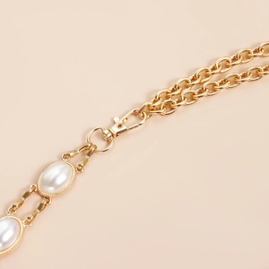 Detail of gold metal chain belt with oval pearls and textured wavy frames with lobster clasp