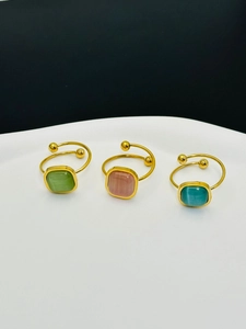 Detalle de tres anillos ajustables de titanio dorado con piedras cuadradas de colores