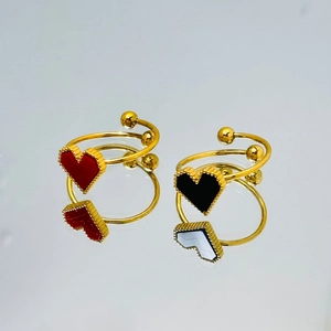 Detalle de anillo dorado ajustable con colgantes de corazón negro y rojo sobre espejo