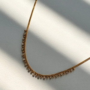 Elegant gold titanium necklace with hanging zircon crystals and beads against soft shadow
