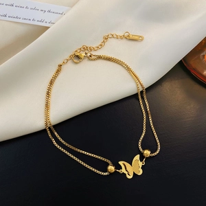 Detalle de tobillera de mariposa en oro de 18k con doble cadena de acero inoxidable