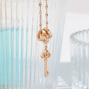 Roségouden titanium ketting met vintage sleutel en drie ringhangers op glazen achtergrond