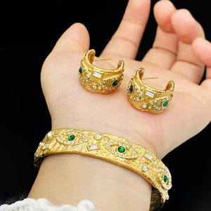 Vintage gold hammer textured evil eye jewelry set with green stones on a black background