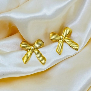 Detail der 18K Gold-Ohrstecker in Schleifenform mit Seidentextur auf Satinhintergrund