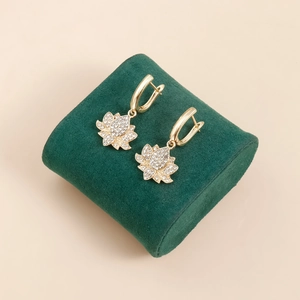Gros plan de boucles d'oreilles lotus dorées avec cristaux blancs sur velours vert