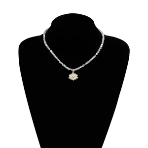 Détail du pendentif lotus doré serti de zircons sur un collier de perles de cristal