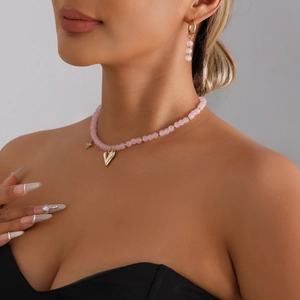 Pink beaded heart pendant necklace and gold earring set worn by a fashion model