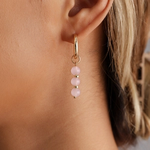 Detail shot of a golden hoop earring with three hanging pink beads and metallic spacers