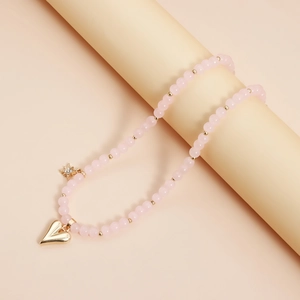 Pink beaded heart necklace with gold star charm displayed on a beige cylinder