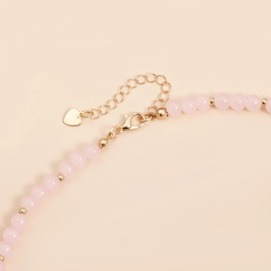 Detailed view of pink beaded necklace featuring a golden lobster clasp and heart charm