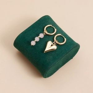 Detail view of asymmetric gold-plated earrings with pink beads and a heart pendant on velvet