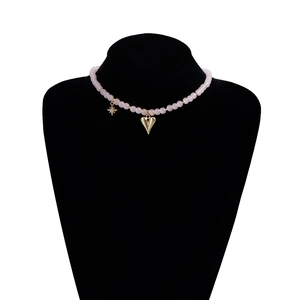 Detail of pink beaded necklace with gold heart pendant and star charm on black velvet stand