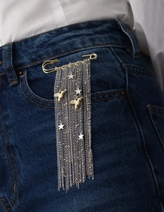 Dettaglio di spilla a nappa con colibrì dorati e stelle d'argento su jeans blu