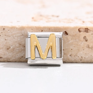 Macro detail of Italian charm bracelet link with gold polished letter M on steel