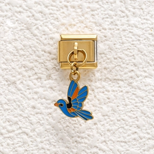Macro view of a gold stainless steel Italian charm featuring a blue enamel bird pendant