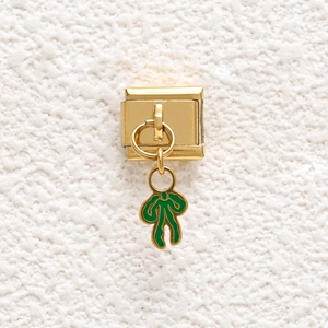 Close-up of golden Italian charm link with green enamel bow pendant on textured white stone