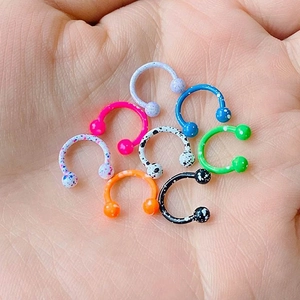 Dettaglio di piercing a ferro di cavallo colorati con effetto spruzzi di vernice in mano
