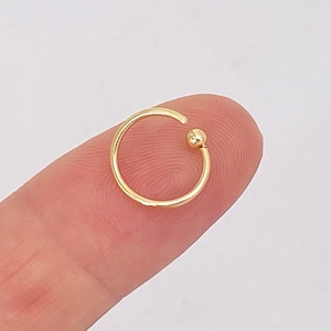Detailed close-up of a small gold captive bead ring for nose or ear piercing on a finger
