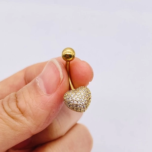 Detalle macro de un piercing de ombligo dorado con forma de corazón y circonitas blancas