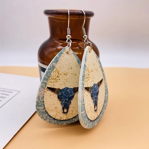 Détail de boucles d'oreilles goutte en cuir avec motif floral longhorn sur flacon ambré