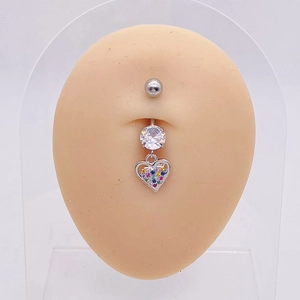 Detalle de piercing de ombligo con corazón plateado y cristales de colores en modelo