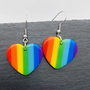 Detailed view of rainbow striped acrylic heart earrings on a dark grey stone pedestal