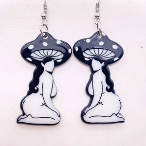 Macro detail of acrylic mushroom girl earrings with surreal black and white artistic charms