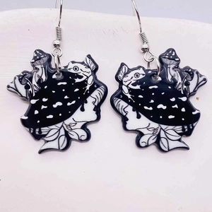 Macro detail of acrylic earrings featuring hand-drawn frog and mushroom illustrations